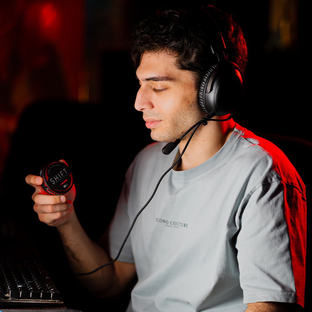Young Man wearing headphone, gaming controller and keyboard in the picture and holding a SHIFT Caffeine box